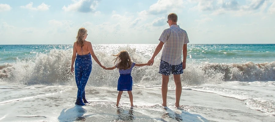 A young family of three holding hands at the beach with a wave crashing in front of them